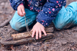 Kind spielt auf Waldboden mit Holz